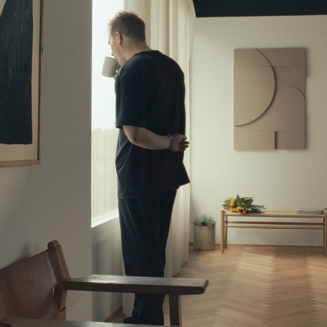Man standing by a window in a calm, minimal space featuring acoustic wall art designed for better room acoustics.