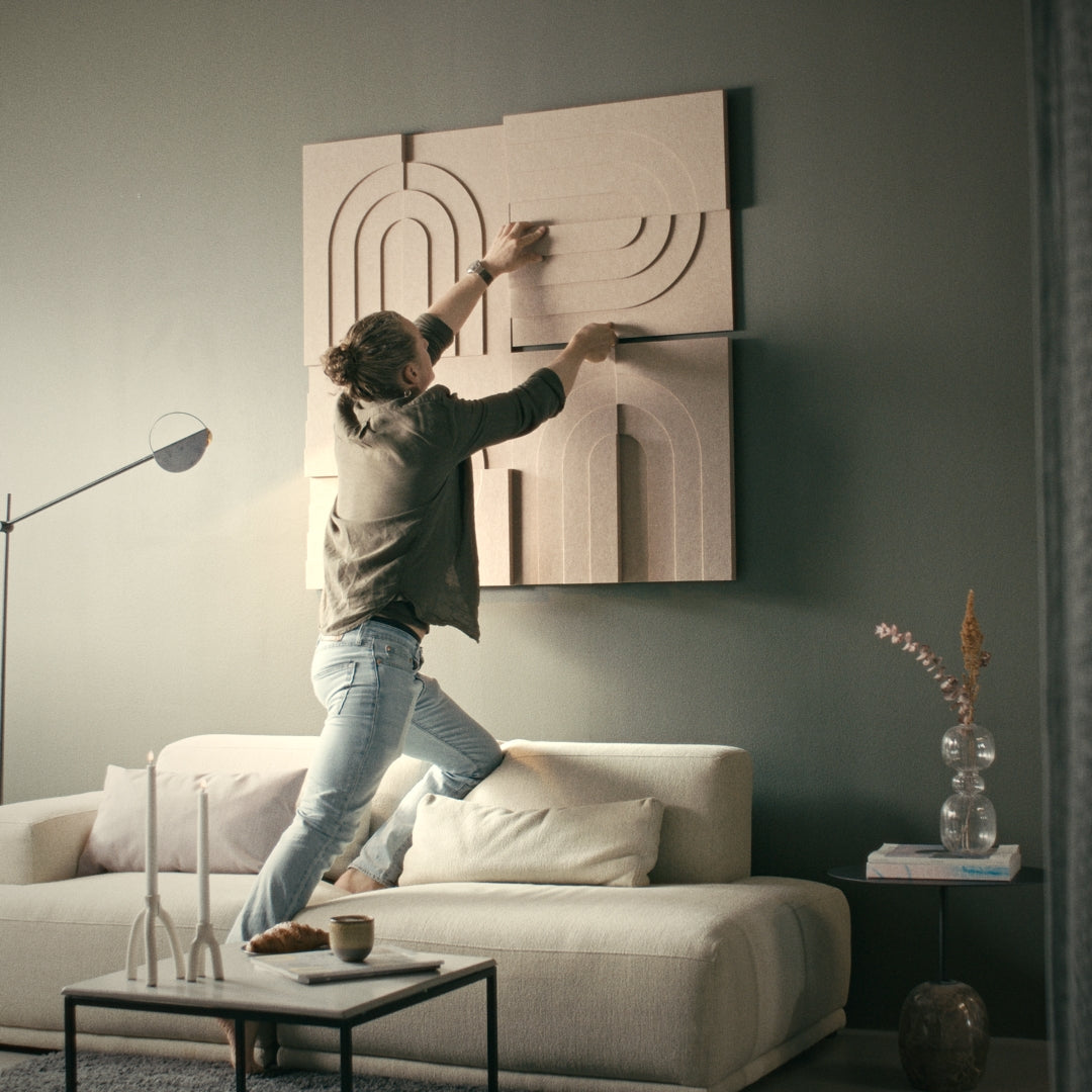 Man adjusting acoustic art panels on a living room wall, improving acoustics in a room with modern sound-absorbing design.